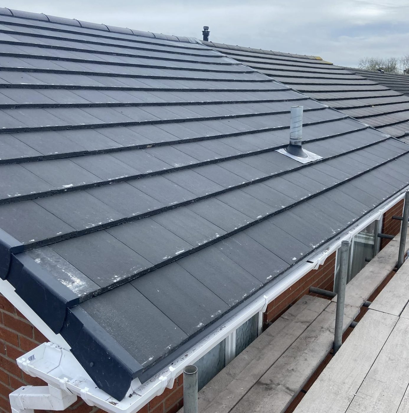 Re-roofed bungalow in grey tiles with dry verge, new vent pipe and white guttering