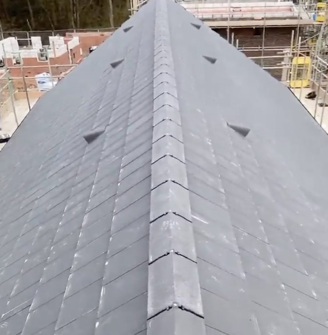 Grey ridge running along a newly slated new-build roof with slate vents