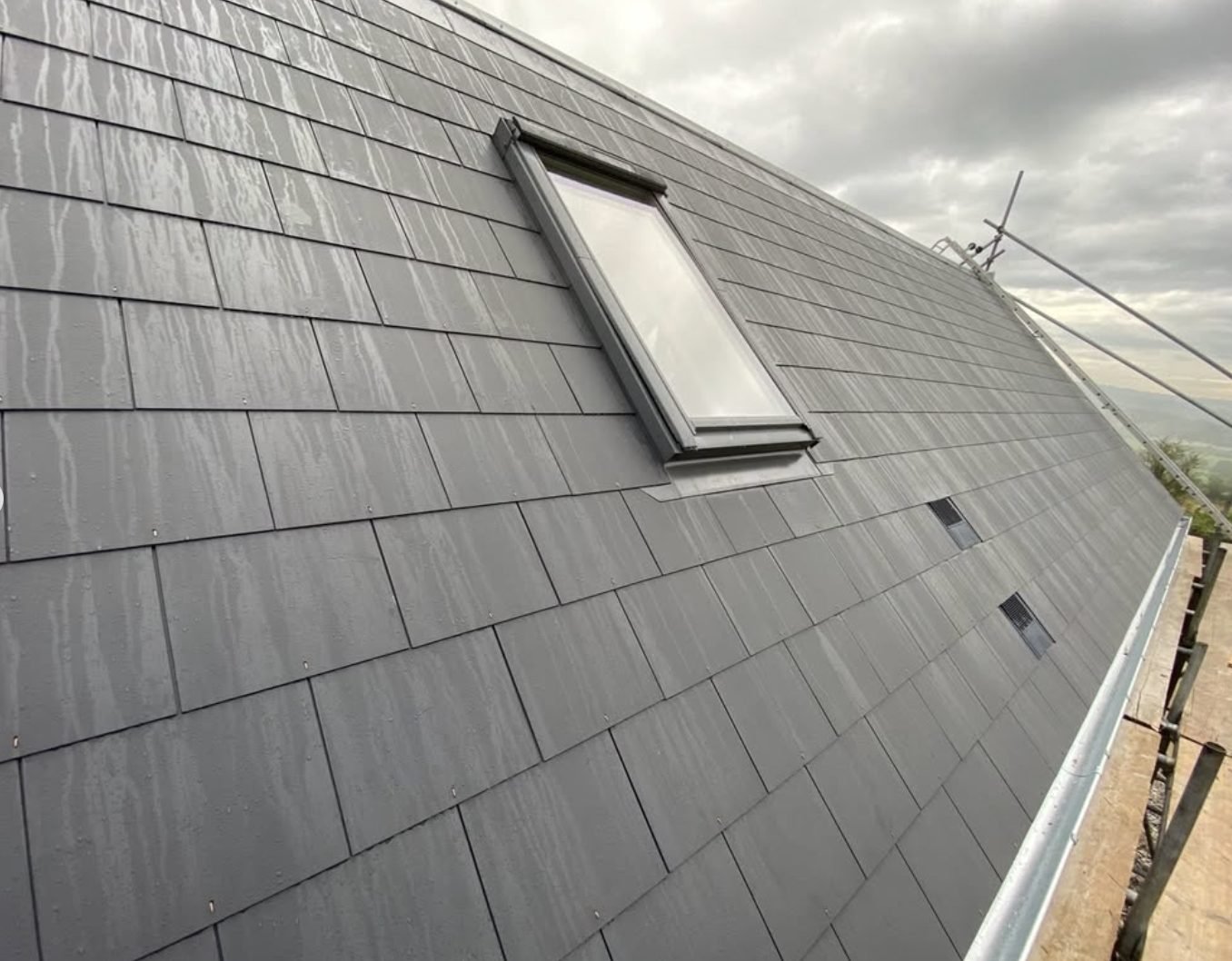 Finished slate roof with a roof window and slate vents, wet after rain