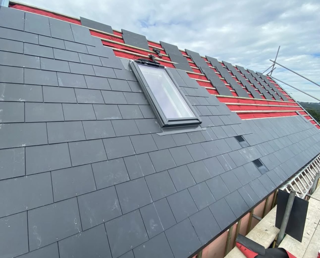 Slates being laid over red membrane and battens around a new roof window